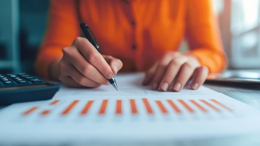 Close-up of a person reviewing and marking a financial report with bar charts at a desk.